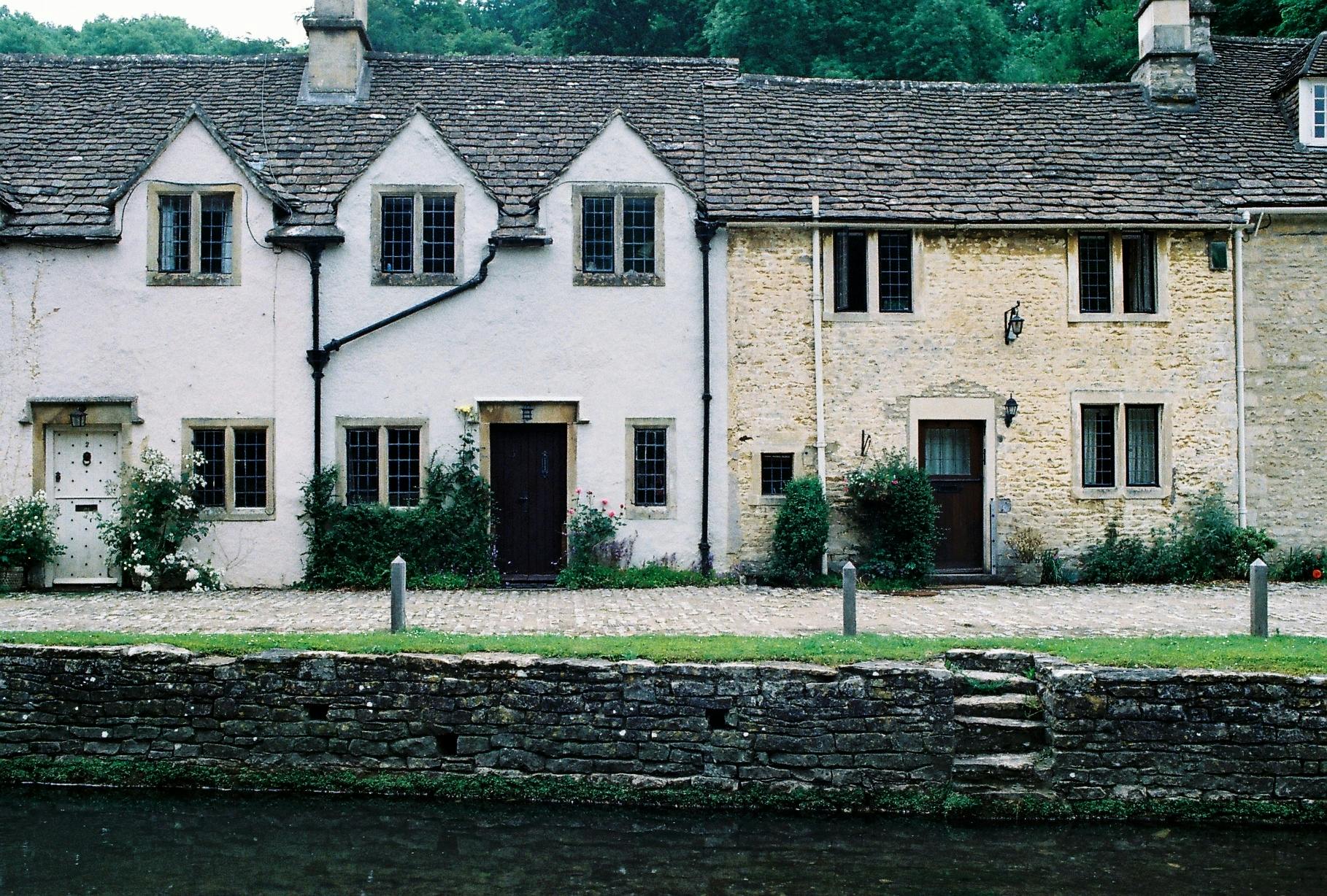 A terrace of old stone and rendered cottages with chimney stacks, beside a river